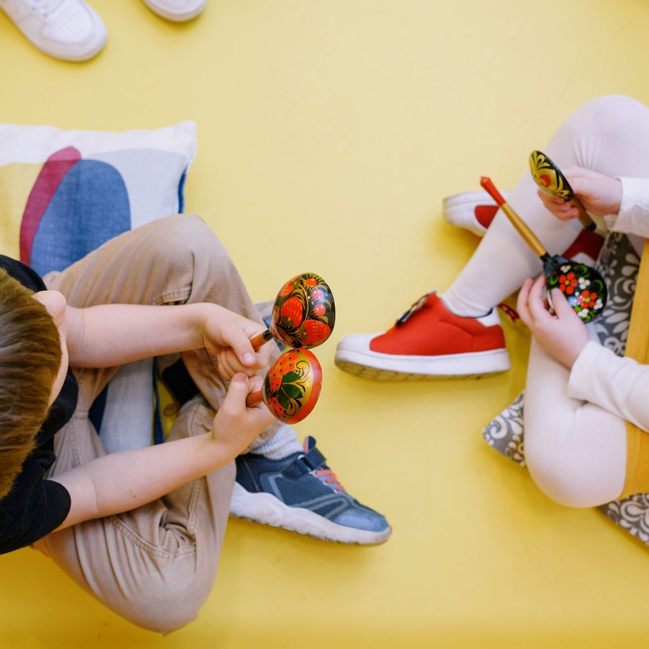Zwei Kinder sitzen auf dem Boden und spielen mit bemalten Rasseln